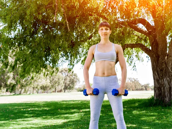 Retrato de mujer alegre en ropa de fitness haciendo ejercicio con mancuerna —  Fotos de Stock