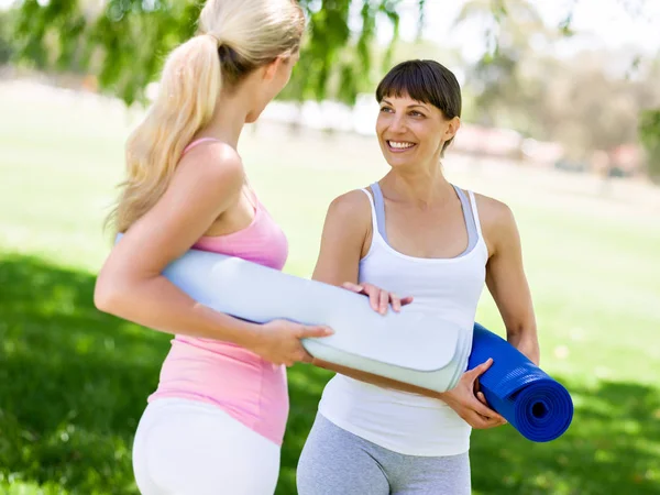 Dos mujeres jóvenes con una alfombra de gimnasio charlando en el parque — Foto de Stock