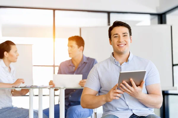 Jonge knappe zakenman met zijn touchpad zitten in kantoor — Stockfoto