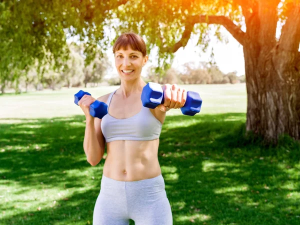 Porträt einer fröhlichen Frau in Fitnessbekleidung, die mit einer Hantel trainiert — Stockfoto