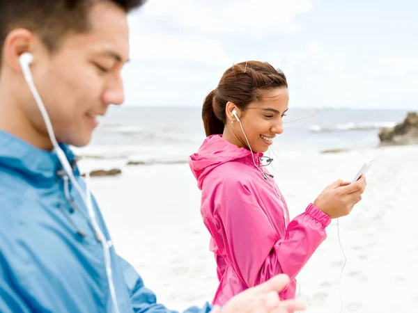 Sportovní mladý pár s sluchátka na pobřeží moře — Stock fotografie