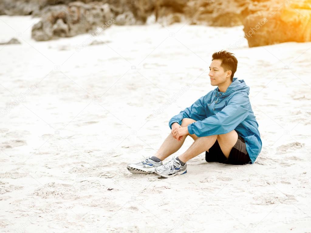 Young man sitting at the beach in sportswear