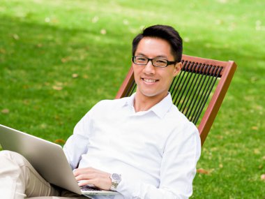 Genç işadamı açık havada otururken dizüstü bilgisayar kullanarak