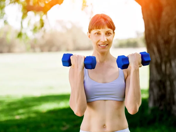 Portrait of cheerful woman in fitness wear exercising with dumbbell — Stock Photo, Image