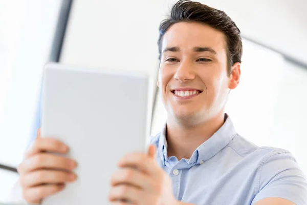 Joven hombre de negocios guapo usando su touchpad sentado en la oficina —  Fotos de Stock