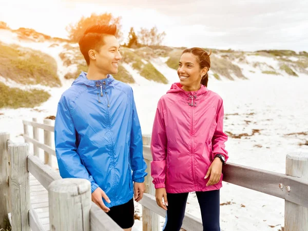 Молодой человек и женщина в спортивной одежде прогуливаются по пляжу — стоковое фото