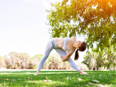 Genç kadın parkta yoga yapıyor.