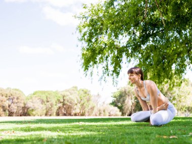 Genç kadın parkta yoga yapıyor.