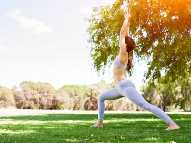 Genç kadın parkta yoga yapıyor.