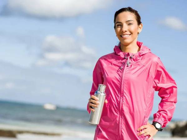 Belle fille en vêtements de sport boire de l'eau après l'entraînement sur la plage — Photo