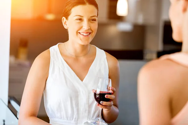 Ung kvinna med hennes vän hålla ett glas vin inomhus — Stockfoto