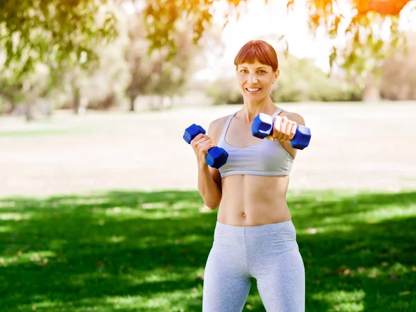 Porträt einer fröhlichen Frau in Fitnessbekleidung, die mit einer Hantel trainiert — Stockfoto