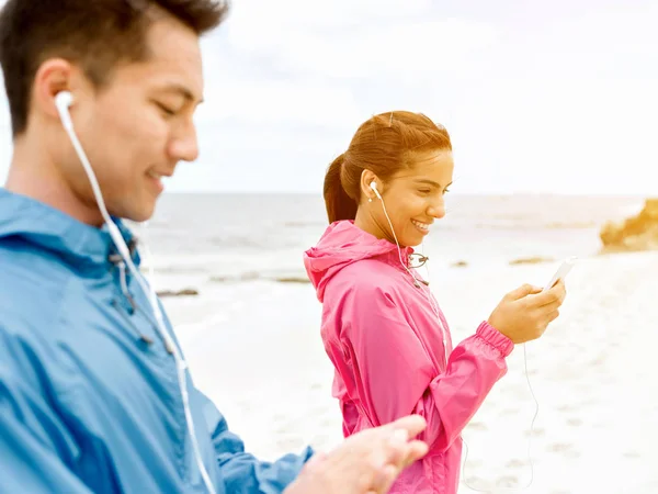Sporty young couple with earphones on the sea coast — Stock Photo, Image