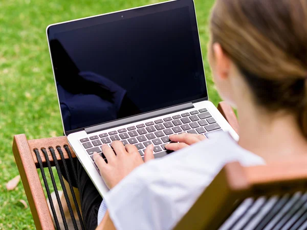 Giovane donna d'affari seduta nel parco e che lavora con il computer portatile — Foto Stock