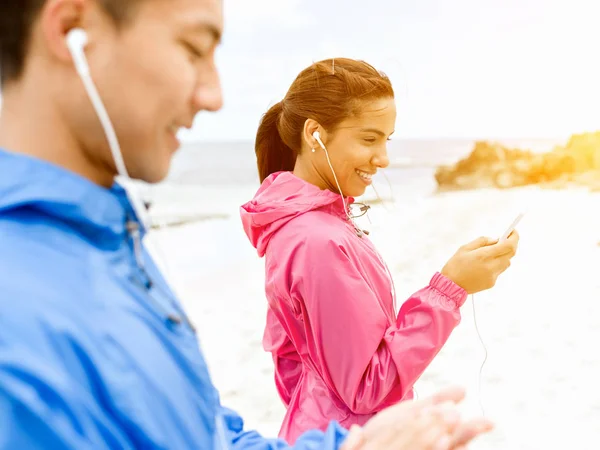 Jeune couple sportif avec écouteurs sur la côte de mer — Photo