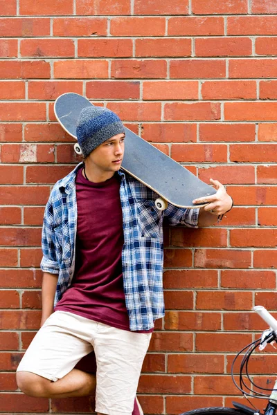 Teenage boy with skateboard standing next to the wall — Stock Photo, Image