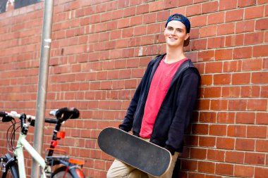 Duvarın yanında durduğunu kaykay ile genç çocuk