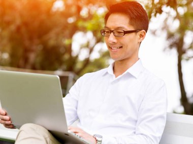 Genç işadamı açık havada otururken dizüstü bilgisayar kullanarak