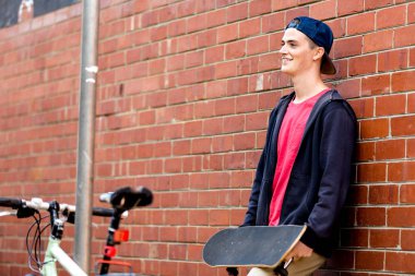 Duvarın yanında durduğunu kaykay ile genç çocuk