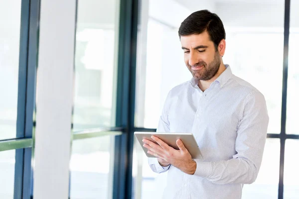 Joven hombre de negocios guapo usando su touchpad de pie en la oficina —  Fotos de Stock