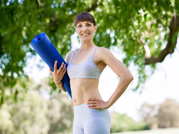 Jonge vrouw witth een sportschool mat in het park — Stockfoto