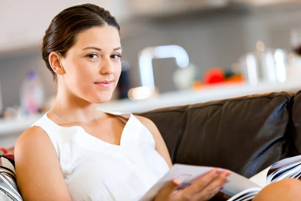 Mujer feliz leyendo una revista sentada en un sofá — Foto de Stock