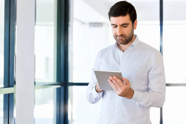 Joven hombre de negocios guapo usando su touchpad de pie en la oficina — Foto de Stock