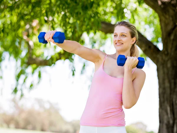 Porträt einer fröhlichen Frau in Fitnessbekleidung, die mit einer Hantel trainiert — Stockfoto