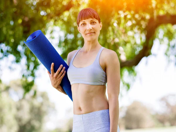 Giovane donna witth un tappetino da palestra nel parco — Foto Stock