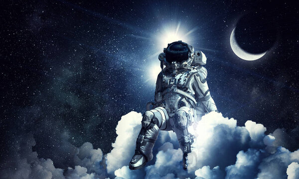 Spaceman sitting on cloud against dark starry sky. Mixed media Elements of this image furnished by NASA