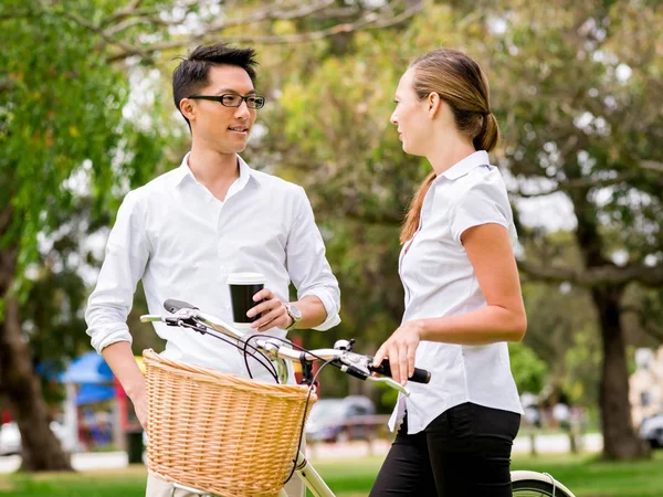 Portrait of smiling couple standing in park with bike talking — Stock Photo, Image