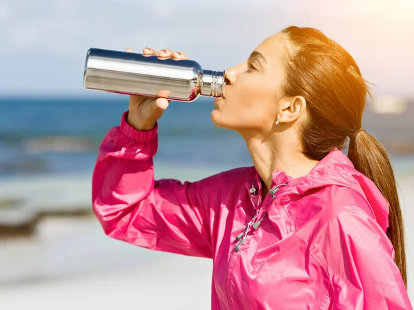 A szép lány a sport ruházat iszik víz edzés után a strandon — Stock Fotó