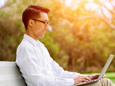 Genç işadamı açık havada otururken dizüstü bilgisayar kullanarak