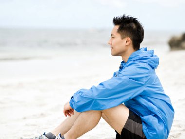 Spor giyim plajda oturan genç adam