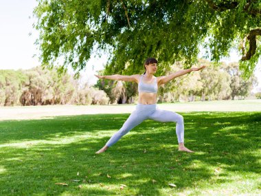 Genç kadın parkta yoga yapıyor.