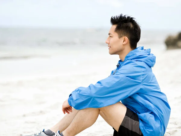 Young man sitting at the beach in sportswear — Stock Photo, Image