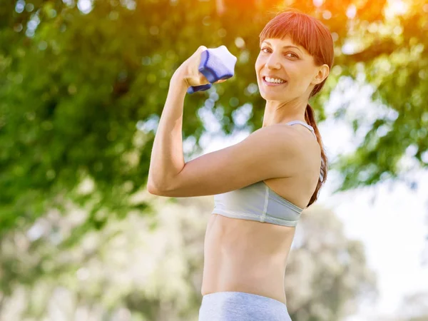 Porträt einer fröhlichen Frau in Fitnessbekleidung, die mit einer Hantel trainiert — Stockfoto