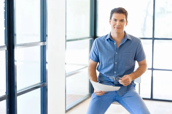 Young business man sitting on a stool in office — Stock Photo, Image