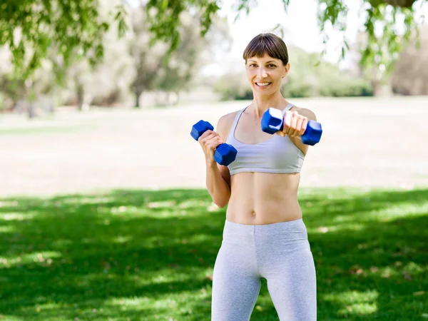 Porträt einer fröhlichen Frau in Fitnessbekleidung, die mit einer Hantel trainiert — Stockfoto