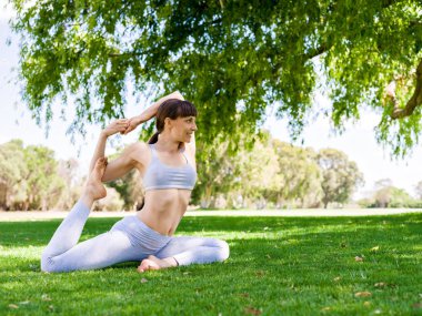 Genç kadın parkta yoga yapıyor.
