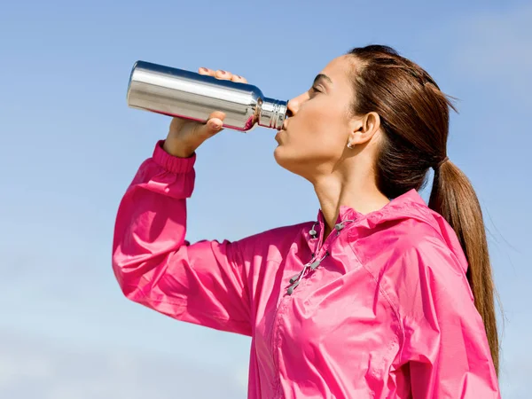 Beautiful girl in sport clothes drinking water after workout on the beach — Stock Photo, Image