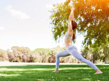 Genç kadın parkta yoga yapıyor.