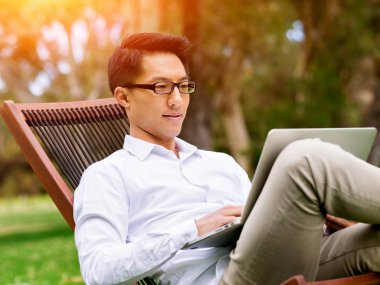 Genç işadamı açık havada otururken dizüstü bilgisayar kullanarak