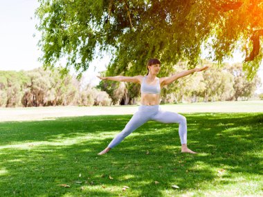 Genç kadın parkta yoga yapıyor.