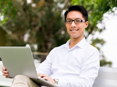 Genç işadamı açık havada otururken dizüstü bilgisayar kullanarak