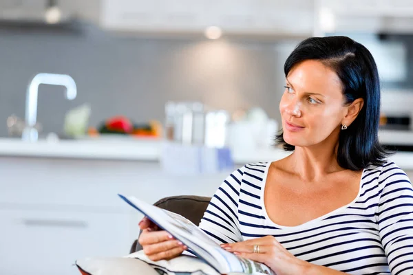 Mulher feliz lendo um livro sentado em um sofá — Fotografia de Stock