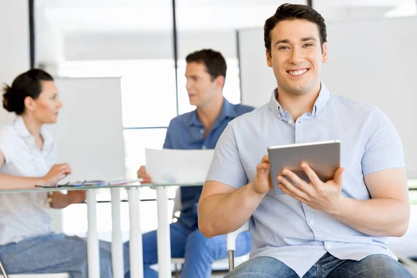 Jonge knappe zakenman met zijn touchpad zitten in kantoor — Stockfoto