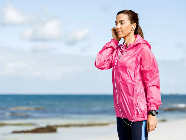 Sportieve vrouw met koptelefoon aan de kust van de zee — Stockfoto