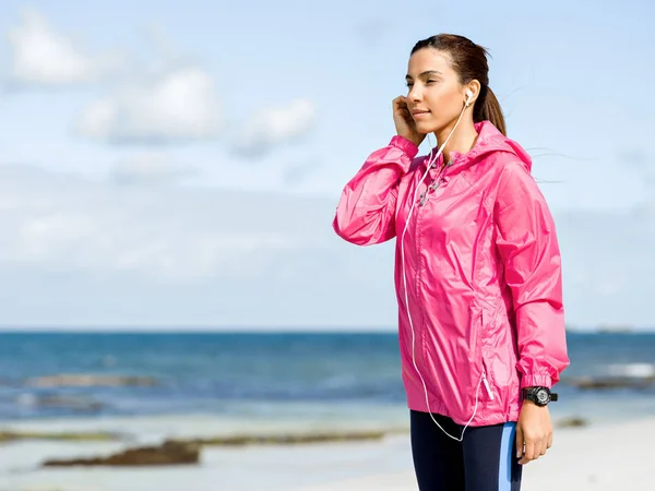 Mujer deportiva con auriculares en la costa del mar —  Fotos de Stock