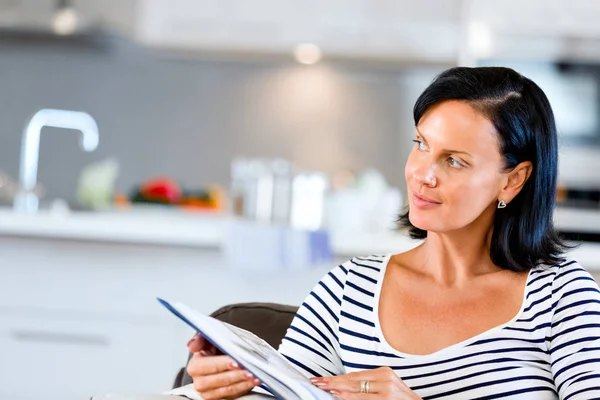 Mulher feliz lendo um livro sentado em um sofá — Fotografia de Stock